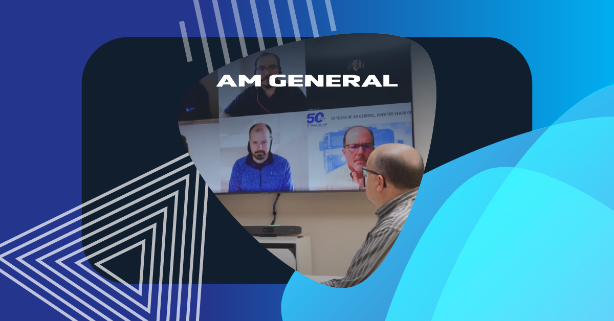 An employee participates in a Microsoft Teams Rooms meeting with AM General colleagues shown on a display in a hybrid meeting setup.